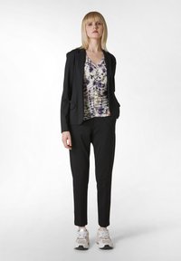 Zwarte blazer over een patroon-top in lichte kleuren met paarstinten, gecombineerd met zwarte tapered broek en lichte sneakers.