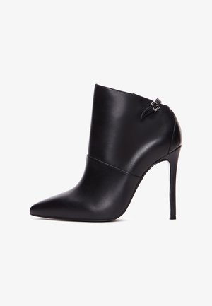 Bottine en cuir noir avec un bout pointu, un haut talon aiguille et une sangle latérale avec une boucle. Texture lisse et design épuré.