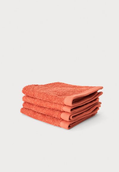Trois serviettes en éponge de couleur corail soigneusement pliées empilées sur un fond blanc.