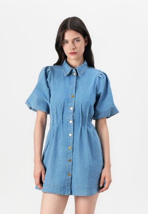 Abito camicia in denim con maniche a palloncino corte, chiusura con bottoni e dettagli plissettati. Di colore azzurro chiaro con bottoni dorati e una silhouette aderente.