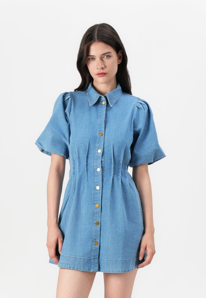Vestido camiseiro de denim com mangas curtas com volume, fecho de botões e detalhes plissados. Cor azul claro com botões em tom dourado e silhueta ajustada.