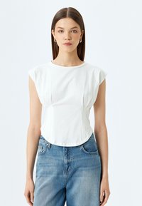 Wit t-shirt met korte mouwen en een ronde halslijn, met een aansluitende pasvorm. Heeft geplooide details en een gebogen zoom. Gepaard met lichtblauwe jeans.
