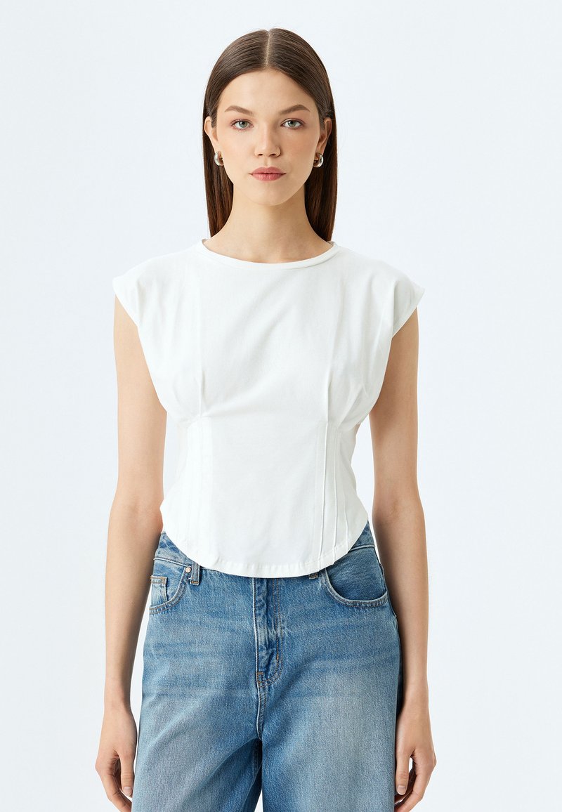 Wit t-shirt met korte mouwen en een ronde halslijn, met een aansluitende pasvorm. Heeft geplooide details en een gebogen zoom. Gepaard met lichtblauwe jeans.