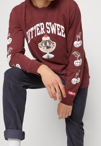 Mörkröd långärmad skjorta med "BITTER SWEET"-text och en glassgrafik på framsidan. Vita körsbärsgrafiker på ärmarna, med Levi's etikett.