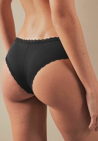 Zwarte panty met kant, afgewerkt met een gladde stof, een hoge snit en een zachte textuur, die een klassieke en strakke silhouet benadrukt.