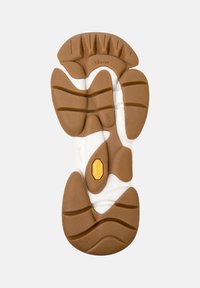 Suela de zapato con banda de rodadura de goma marrón y blanca, surcos profundos para tracción y logo de Vibram en el centro para agarre y durabilidad.