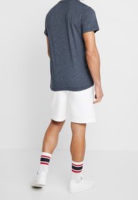 Camiseta de manga corta en tonos azul marino, pantalones cortos blancos y calcetines de rayas multicolores. Diseño minimalista con un corte relajado y una textura suave.