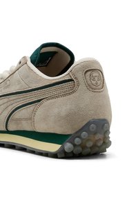 Sneaker in suede beige con dettagli verdi, collo imbottito e suola testurizzata con tacchetti circolari trasparenti per una presa ottimale. Logo embossato sul tallone.