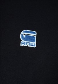 Tessuto nero con un logo ricamato e strutturato che presenta le lettere "S" e "RAW" in azzurro chiaro e bianco.