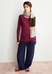 Gestreiftes Langarmoberteil in Rot und Marineblau, kombiniert mit weiten marineblauen Hosen und einem braun-beigen Schal. Die Schuhe besitzen rote Akzente und Schnürsenkel.