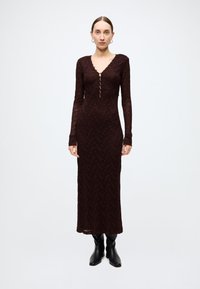 Burgundy long-sleeve lace dress with a V-neck, featuring a button front and a streamlined silhouette, paired with black ankle boots.