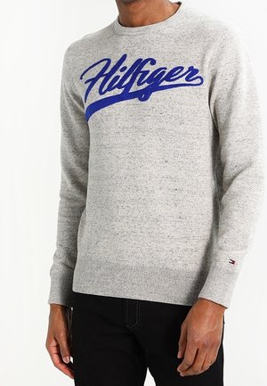 Suéter de punto gris con cuello redondo, que presenta un logo bordado azul "Hilfiger" en el pecho. Detalle de puños y dobladillo en canalé.