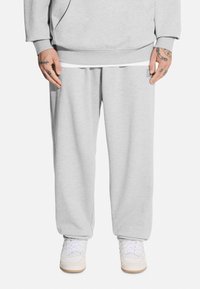 Jasnoszare dresy wykonane z miękkiego materiału, o luźnym kroju, z elastyczną talią i bocznymi kieszeniami, w zestawie z białymi sneakersami.