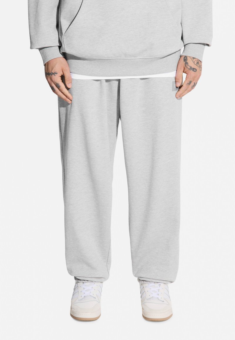 Jasnoszare dresy wykonane z miękkiego materiału, o luźnym kroju, z elastyczną talią i bocznymi kieszeniami, w zestawie z białymi sneakersami.