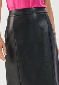 Vrouw in een hoog- Taille zwarte leren rok en een felroze top die in de rok is gestopt, zichtbaar van halverwege de dij tot aan de taille.