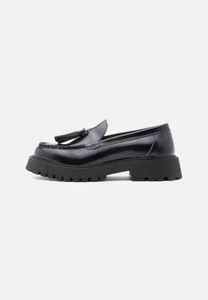 Black leather loafers with a tapered design, tassel accent, and chunky rubber sole featuring a lug pattern for traction.
