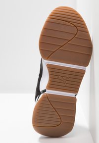 Schwarzer Sportschuh mit einer strukturierten Gummisohle, weißem Mittenboden und einer braunen Gummisohle mit horizontalen und diagonalen Rillen.