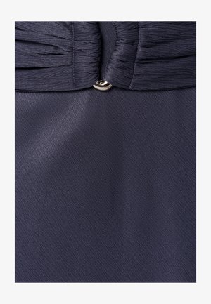 Tmavomodrá plisovaná látka zhromaždená s malým strieborným gombíkom v strede, zobrazujúca textúru a švíky.