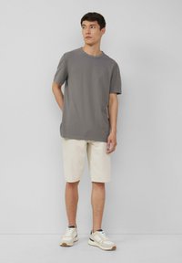 Grijze t-shirt met korte mouwen en een ronde hals, gecombineerd met beige shorts en witte sneakers. Subtiele logo op de borst, eenvoudig ontwerp.