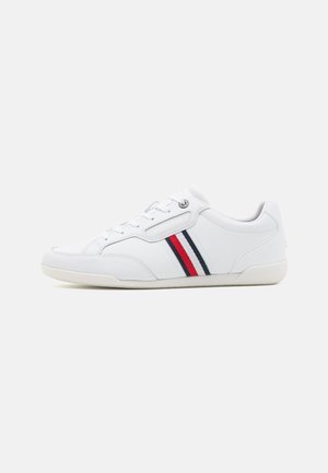Białe sneakersy z gładkiego materiału syntetycznego, okrągłym kształcie, sznurowanej konstrukcji oraz trzema poziomymi paskami w kolorach czerwonym, białym i niebieskim.