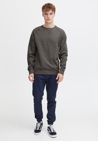 Mørkegrå crewneck sweatshirt med ribbede manchetter, parret med navy tapered bukser og sorte sneakers med hvide detaljer. Enkel, afslappet design.