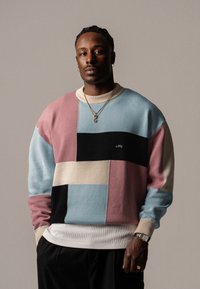 Maglione a blocchi di colore con tonalità pastello di blu, rosa, nero e beige. Texture a maglia con colletto e polsini a coste. Dettaglio logo ricamato.