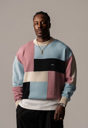 Color-blocked sweater featuring pastel shades of blue, pink, black, and beige. Knit texture with a ribbed collar and cuffs. Logo embroidered detail.