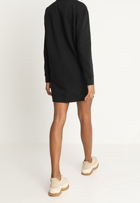 Black sweatshirt dress with long sleeves, loose fit, reaching mid-thigh, paired with chunky beige sneakers featuring a textured sole.