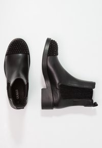 Bottines noires en cuir avec un panneau en tissu noir texturé et un accent clouté sur le bout. Talon plat et côtés en élastique pour un enfilage facile.