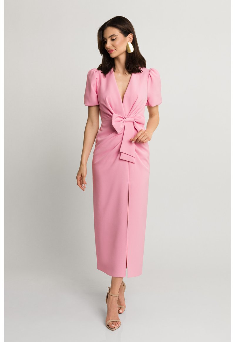 Różowa sukienka do kolan z bufiastymi rękawami, głębokim dekoltem w kształcie litery V, z przodu z kokardą i rozcięciem na udzie. Gładki materiał o dopasowanym kroju.