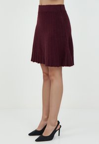 Burgunderfarbene gerippte Strickskirt mit ausgestellter Form, tailliertem Bund und strukturiertem Finish. Kombiniert mit schwarzen spitzen Absätzen.