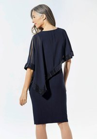 Robe navy avec un superposé en chiffon fluide, ornée d'accents en sequins le long des bords. Le design comprend des manches courtes et une silhouette ajustée.