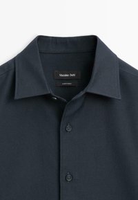 Ciemnogranatowa koszula z guzikami, z wyraźnym kołnierzykiem, wykonana z jednolitego materiału. Zawiera dwa widoczne guziki oraz metkę z napisem "Massimo Dutti, Wyprodukowano w Turcji."