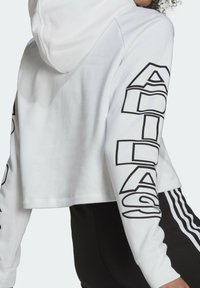 White cropped hoodie with a hood, featuring large black "ADIDAS" text on sleeves. Made of smooth fabric with long sleeves and a relaxed fit.