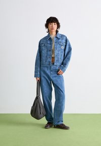 Veste en denim bleu clair et pantalon avec un motif subtil, accompagnés d'un haut vert clair. Accessoire : sac à épaule gris à motifs. Chaussures brunes.