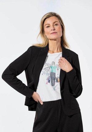 Schwarzes Blazer mit langen Ärmeln, figurbetontem Design, kombiniert mit einem weißen T-Shirt, das eine farbenfrohe Einkaufsgrafik zeigt, und lässigen schwarzen Hosen.