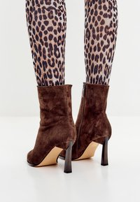 Bruine suède enkelboots met een strakke uitstraling, hoge stiletto-hakken en een zijritsdetail, gecombineerd met leggings met panterprint.