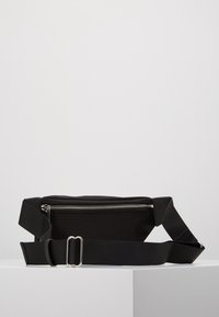 Zwarte stoffen heuptas met een gladde textuur, voorzien van een zilveren rits, een verstelbare schouderriem en een rechthoekige vorm.