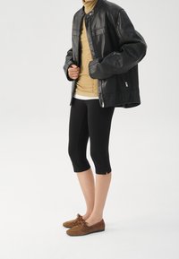 Zwarte leren jas, beige coltrui, zwarte cropped leggings en bruine suède schoenen met veters. Eenvoudig ontwerp en een getailleerde pasvorm.