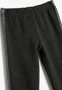 Leggings grises hechos de un material suave con una cinturilla elástica, que presentan una franja lateral plateada brillante y una textura sutil.