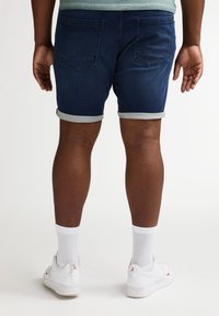 Pantalones cortos de mezclilla en azul oscuro con dobladillos enrollados, que cuentan con dos bolsillos traseros. Se llevan con calcetines blancos hasta el tobillo y zapatillas blancas.