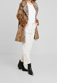 Abrigo de estampado de leopardo con textura de pelo sintético, cuello oversize, combinado con jeans blancos y botas de tobillo negras. El abrigo tiene un diseño de media longitud.