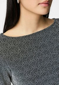 Juoda palaidinė su smulkiais baltais taškeliais tekstūruotame rašte. Iškirptė plati, valtimi primenanti. Audinys atrodo lengvas ir lygus.