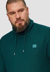 Turquoise sweatshirt met een hoge kraag, voorzien van een gestructureerd oppervlak, verstelbare koordjes en een klein logo-opdruk op de borst.