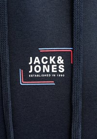 Laivastonsininen collegepaita, jossa on valkoinen logo "JACK & JONES" ja teksti "ESTABLISHED IN 1990" sekä punaiset ja siniset korostusviivat.
