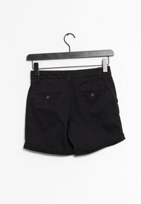 Shorts en coton noirs avec un ourlet retourné, dotés de deux poches arrière avec fermetures à bouton, présentés sur un cintre noir sur fond blanc.