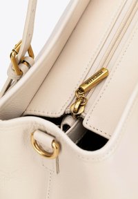 Borsa a mano in pelle crema con hardware dorato, zip superiore e nome del marchio in rilievo sul tirante della zip. Texture liscia e design strutturato.