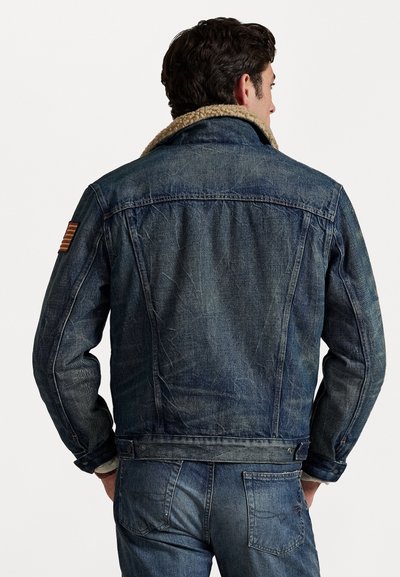 Denimtakki, jossa on vaaleanbeige sherpa-kaulus, takana yoke-yksityiskohta ja vasemmassa olkapäässä punavalkea raidallinen lippu.