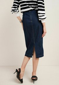 Gonna a matita in denim scuro con spacco centrale sul retro, cuciture a contrasto e silhouette aderente. Indossata con una maglia a righe bianca e nera.