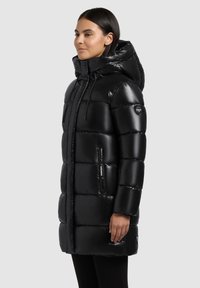 Sort dunjakke med en blank finish, stor hætte, lynlåslommer, quiltet design og snoretræk ved halsen.